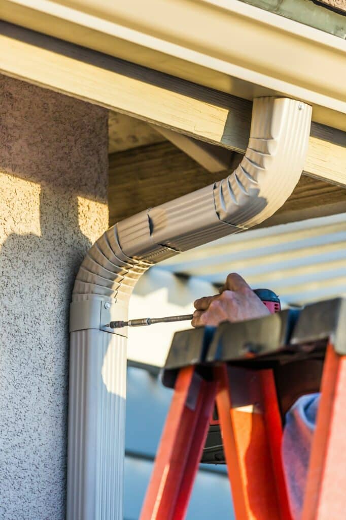 Worker Attaching Aluminum Rain Gutter and Down Spout to Fascia of House